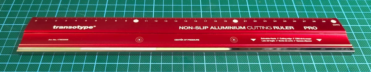 A red aluminum-body Transotype non-slip cutting ruler lying on a green cutting mat.