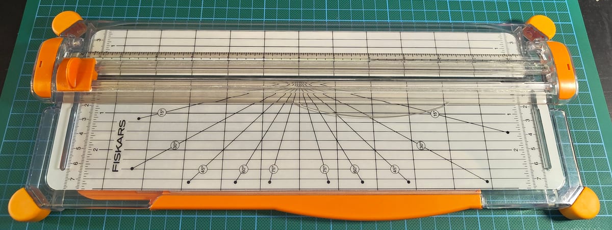 A Fiskars SureCut paper trimmer on a green cutting mat, with the alignment grid and orange end caps visible.