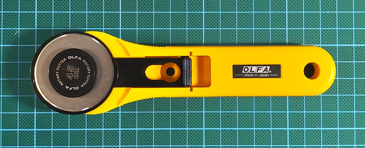 A yellow-handled OLFA rotary cutter on a green cutting mat.