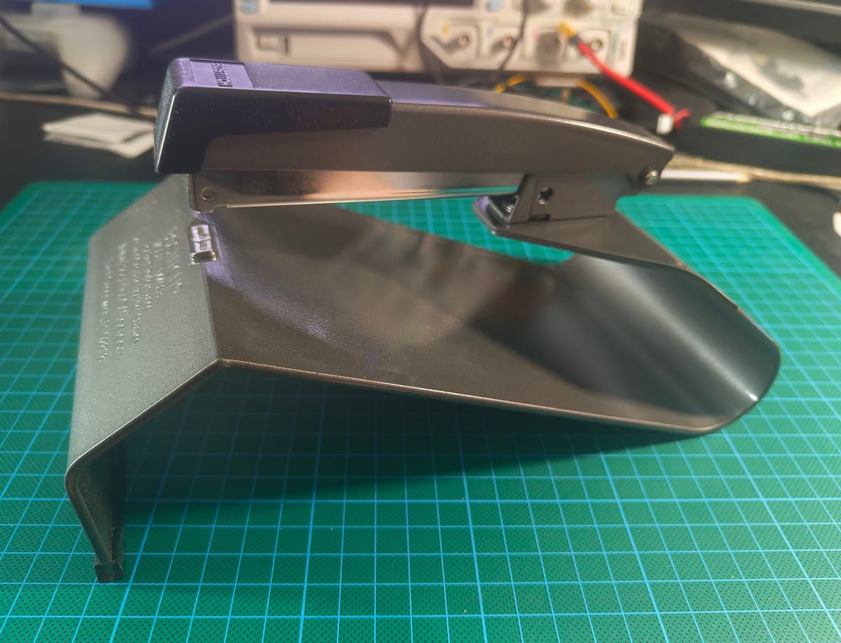 A side view of a dedicated saddle stapler showing its flared V-shaped saddle base on a green cutting mat.