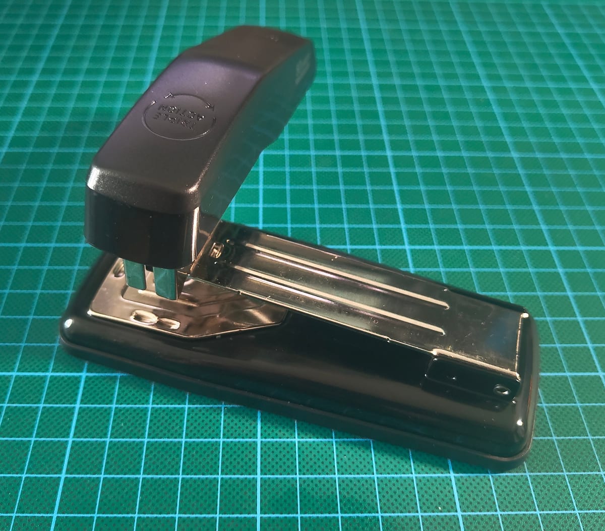 A black 90-degree swivel stapler on a green cutting mat, with the head rotated to expose the ejection point.